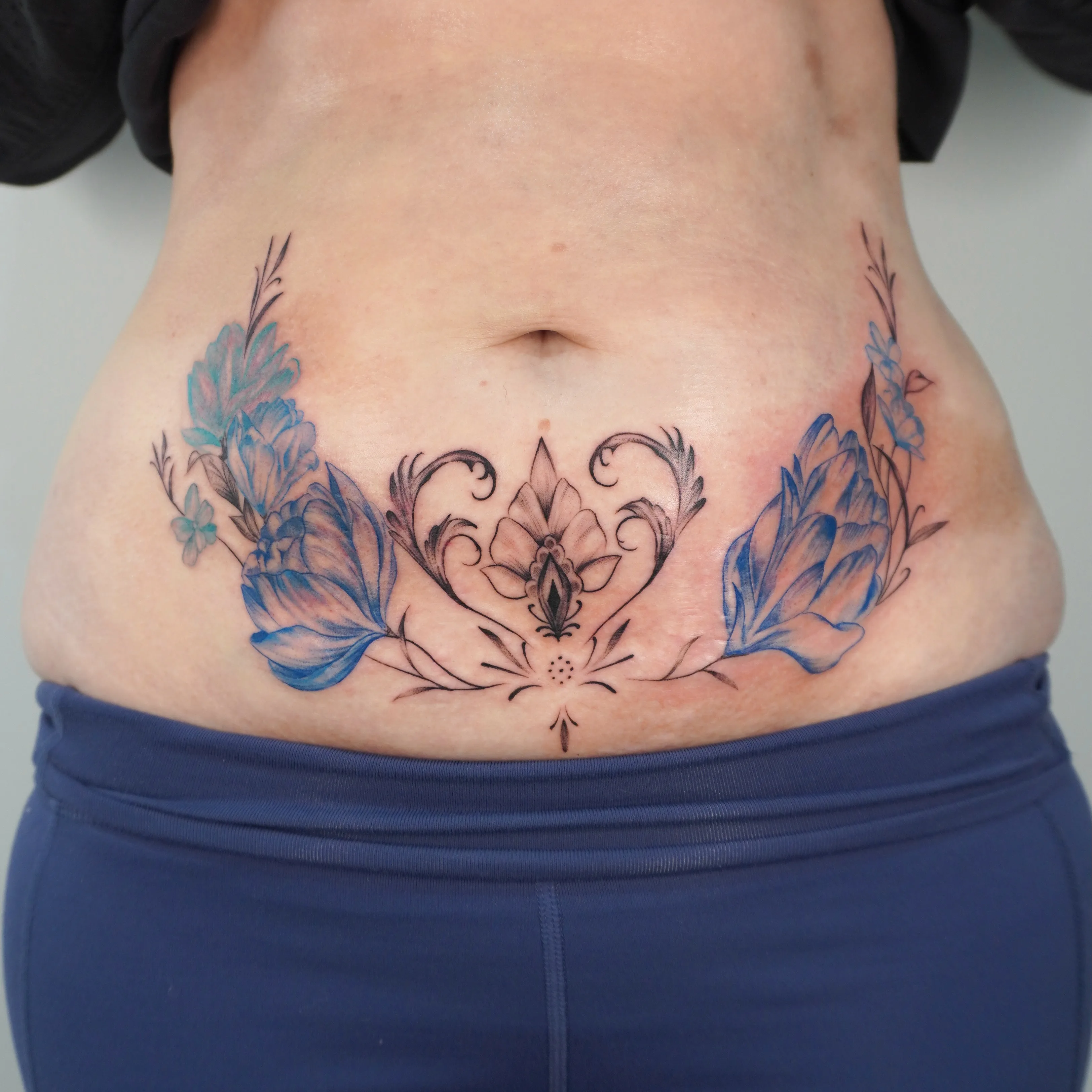 Blue-wash floral and filigree tattoo on the lower abdomen
