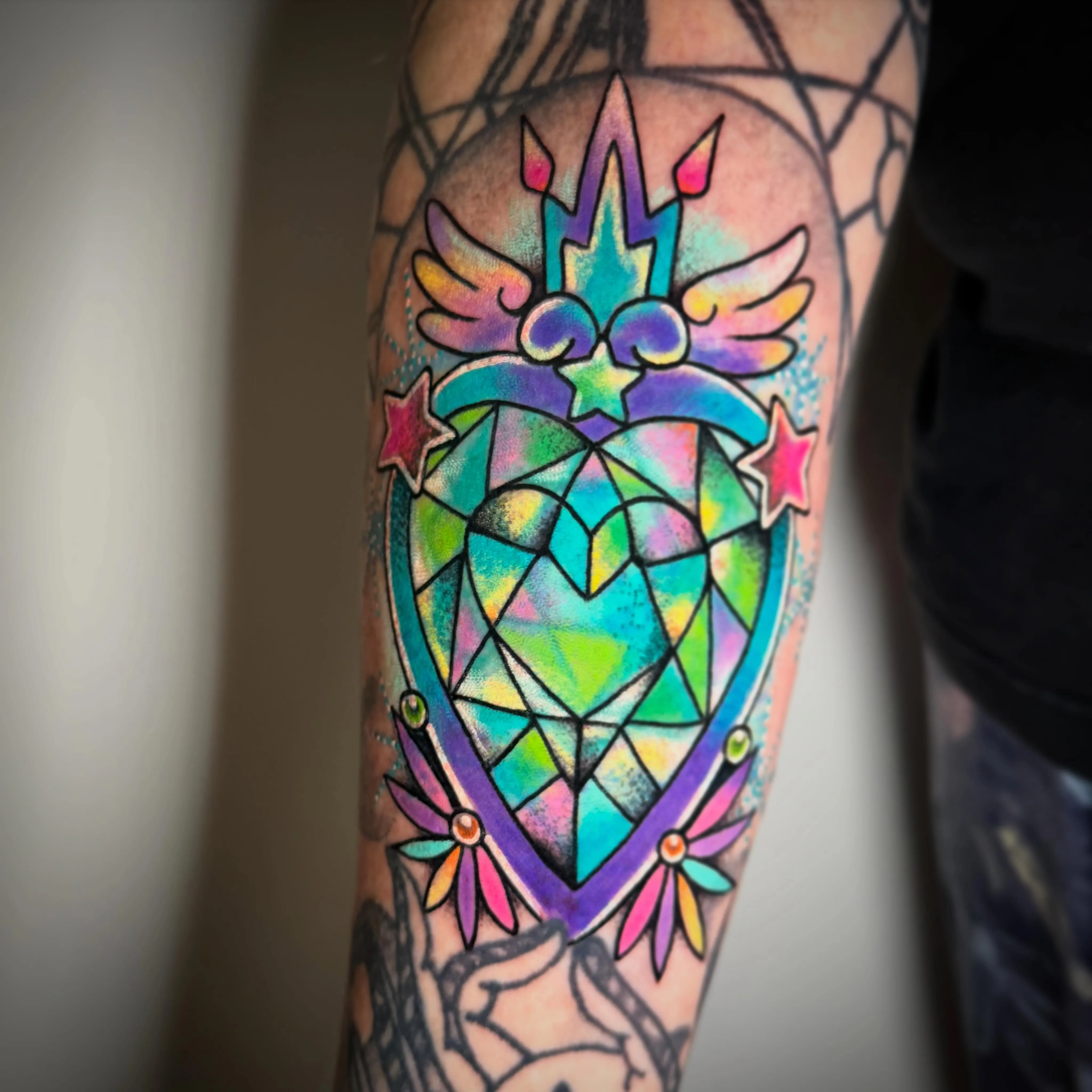Vivid neo-traditional colour tattoo — crowned sacred heart with wings and stars