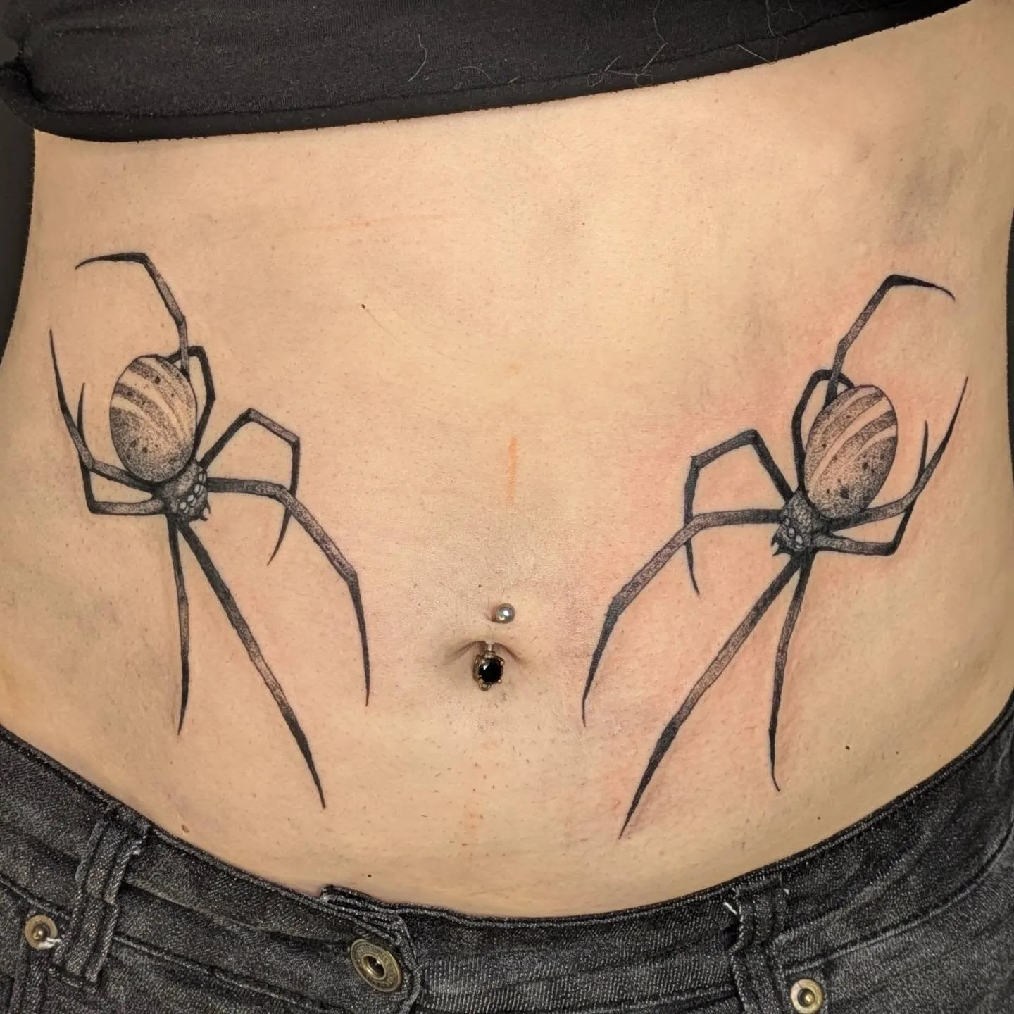 Matched realistic spider tattoos either side of the navel