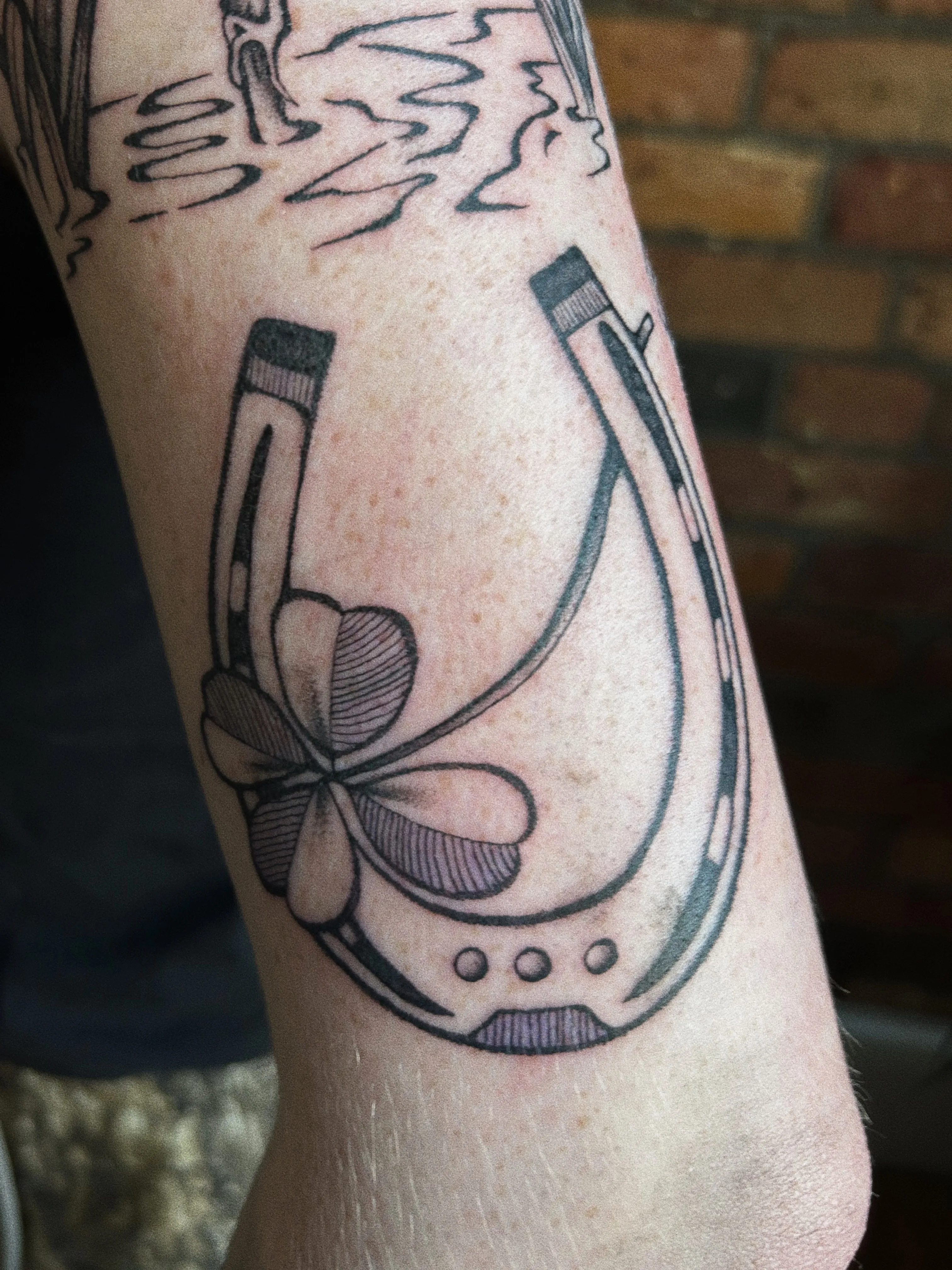 Black and grey leg tattoo — lucky horseshoe with four-leaf clover