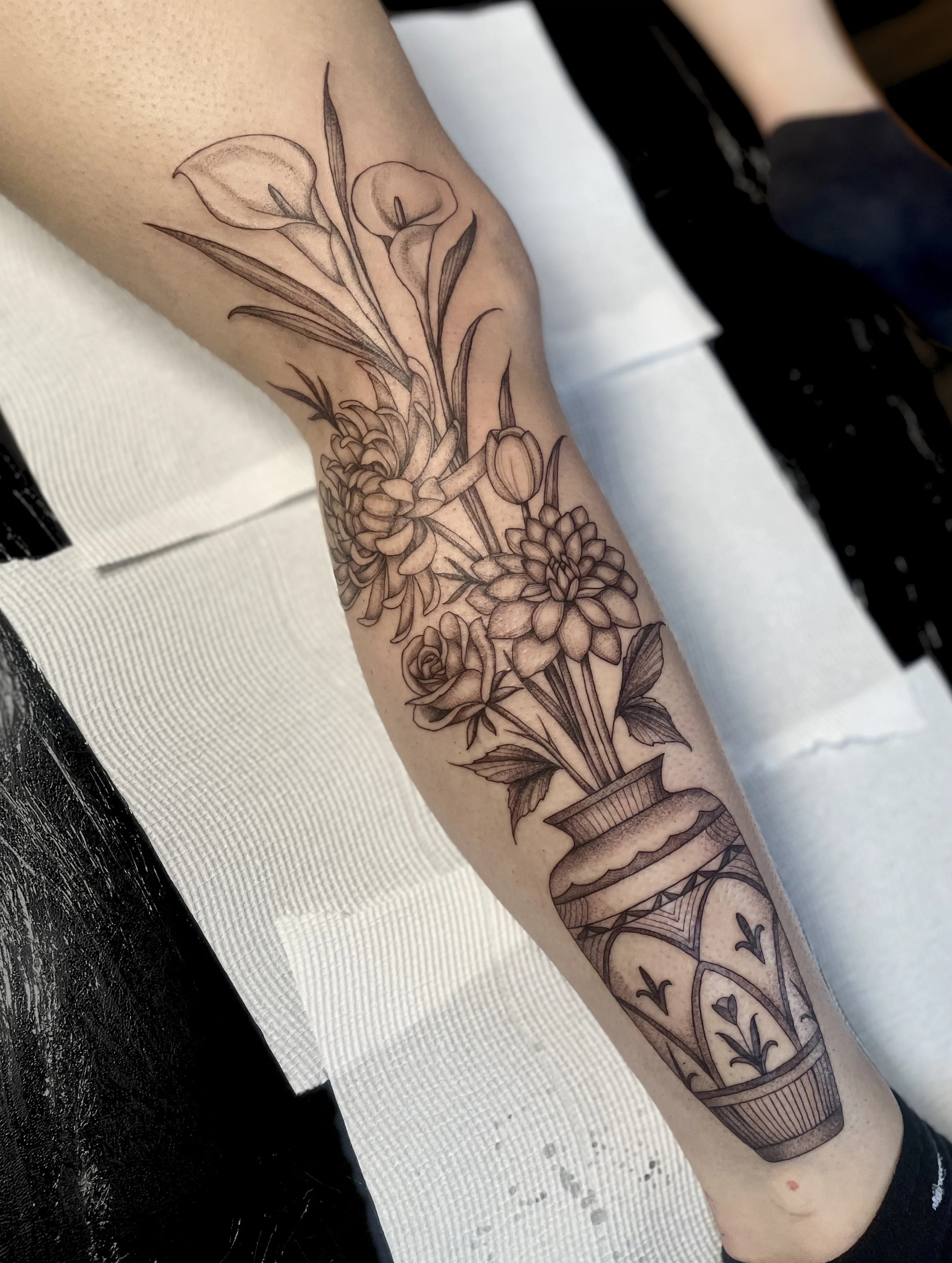 Fine-line black and grey lower-leg tattoo — floral urn with calla lily and rose